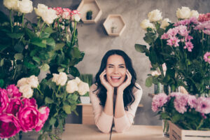 Portrait of her she nice attractive lovely sweet charming cute cheerful cheery glad comic childish wavy-haired lady fooling licking lips among hydrangeas chrysanthemums concrete wall indoors workplace.
